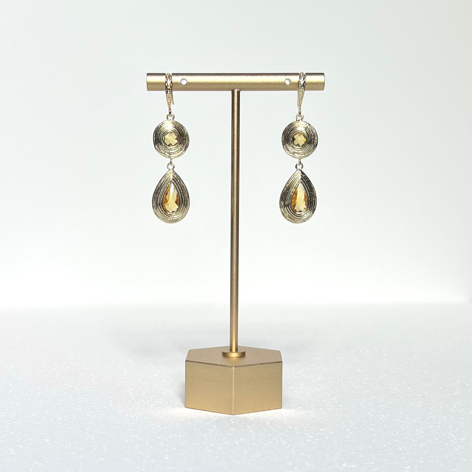 This pair of earrings features a round and teardrop shaped gold charm with citrine color glass centers held by a gold filled French hook.