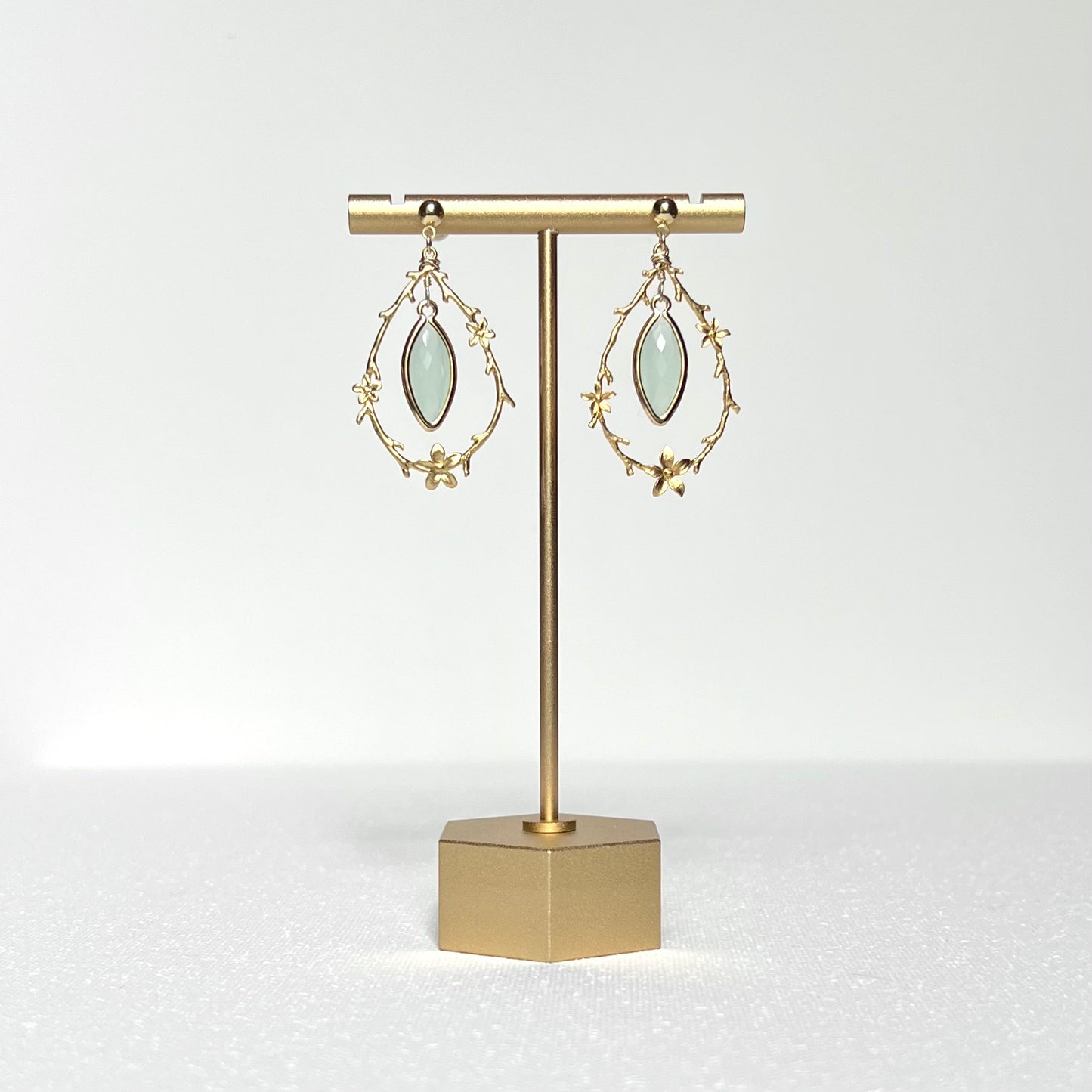 This earring set features a gold branch &amp; flower hoop in which hangs a minty green glass marquise shaped bezel set charm, hung on a gold filled 4mm ball stud earring post.&nbsp;